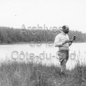 L&rsquo;abb&eacute; Maurice Proulx mange, pr&egrave;s d&rsquo;un lac, lors du tournage de En pays neufs en Abitibi